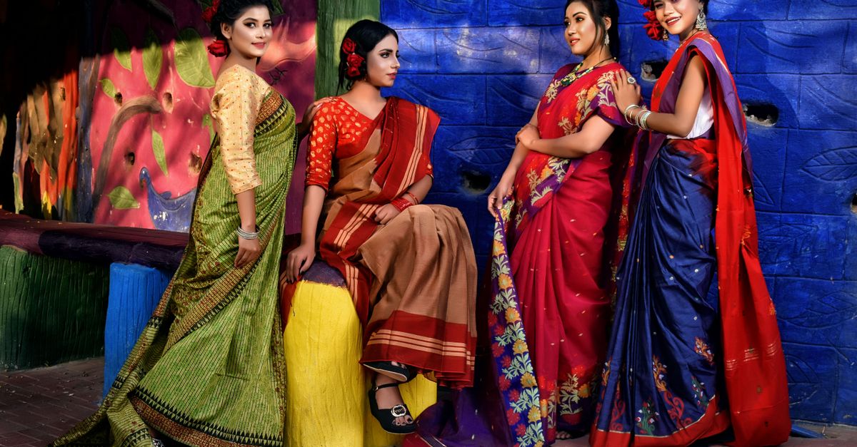 Group of women in vibrant Indian sarees posing against a colorful backdrop.